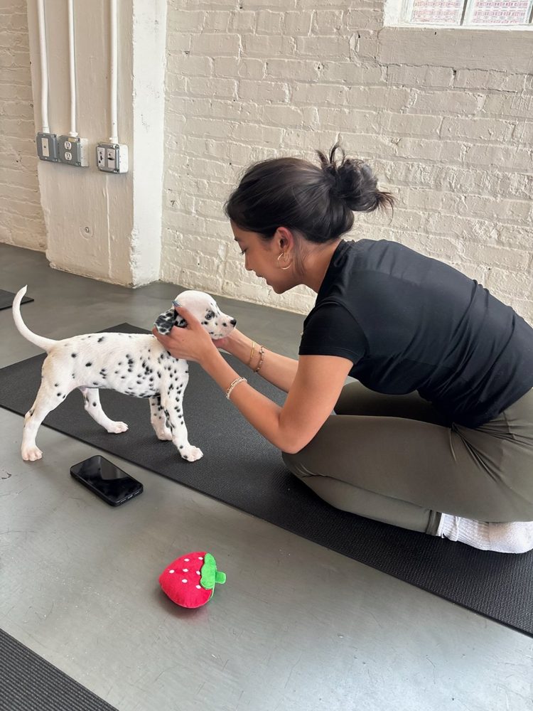 Ashmi kneeling on a yoga mat, petting a Dalmatian puppy